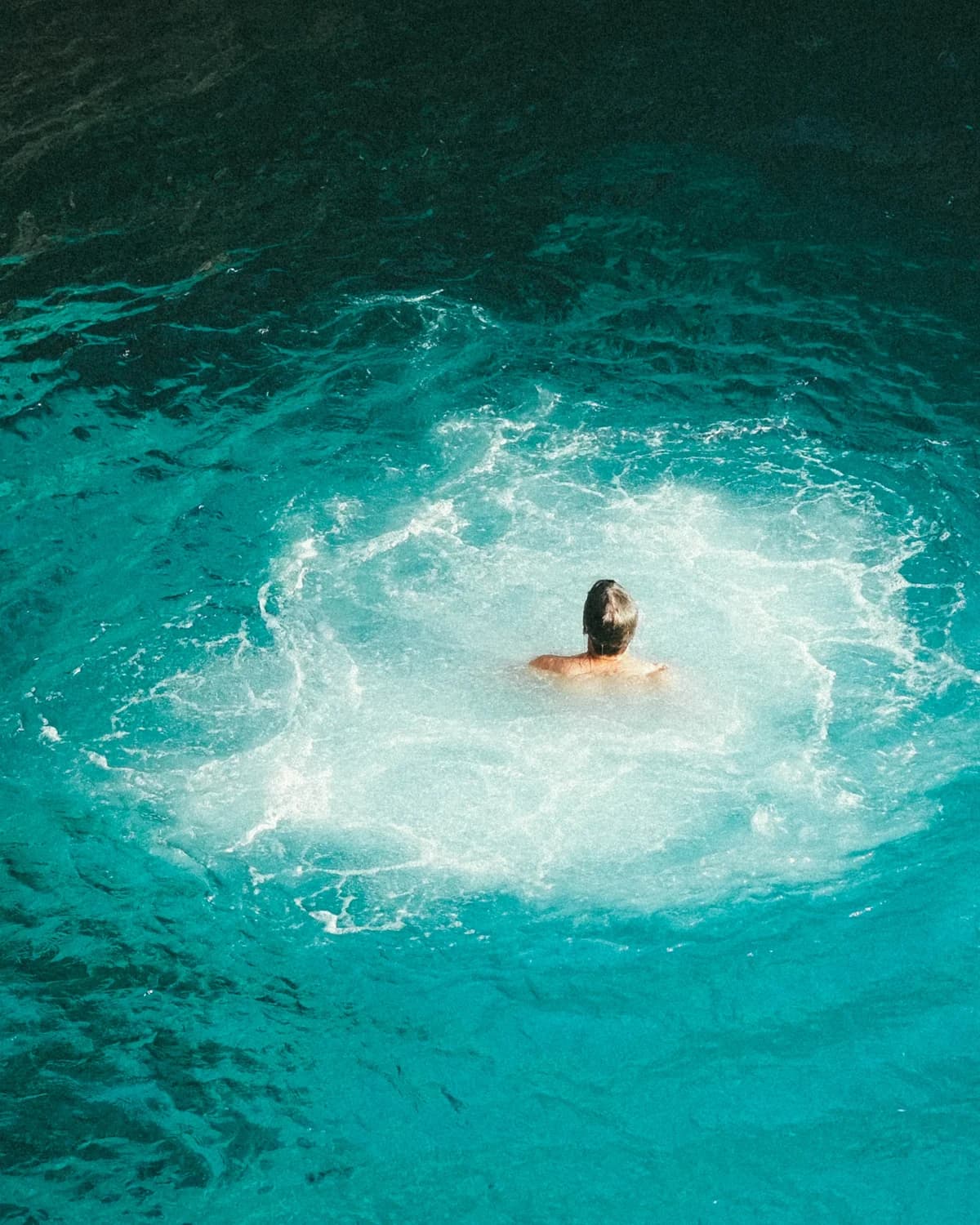 A swimmer surfacing in clear turquoise water below the cliffs at Negril's West End